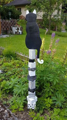 a black and white cat statue sitting in the middle of a garden next to flowers