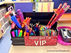 a box filled with lots of colorful pens and pencils on top of a desk