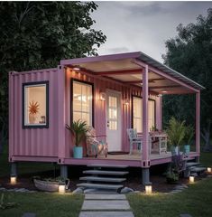 a pink container home with steps leading up to the front door and patio area, lit by candles