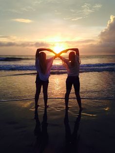 two women are standing on the beach with their arms in the shape of a heart