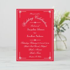 a red and white wedding card on a table next to a vase filled with flowers