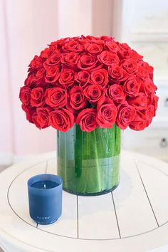 a vase filled with red roses sitting on top of a table next to a candle