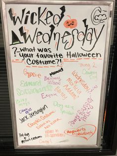 a white board with writing on it in front of a store window that has halloween written all over it