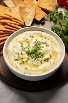 a white bowl filled with dip surrounded by crackers, tomatoes and cilantro