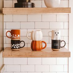 three coffee mugs sitting on top of a wooden shelf next to a white brick wall