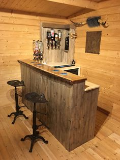 a bar with two stools in a room that has wood paneling on the walls