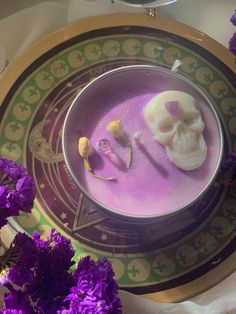 a bowl filled with purple liquid and two skulls on top of it next to purple flowers