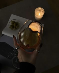 a person holding a wine glass with some olives on the table next to it