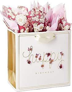 a gift bag filled with pink flowers on top of a white table next to a card that says happy birthday