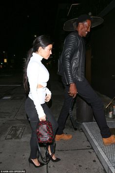 a man and woman walking down the street at night with one carrying a handbag