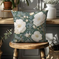 a white flowered pillow sitting on top of a wooden chair next to a potted plant