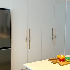 a stainless steel refrigerator in a kitchen next to white cabinets and cutting board with fruit on it