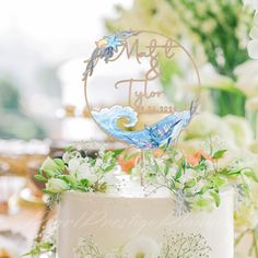 a wedding cake with white flowers and greenery on top is decorated with a blue bird