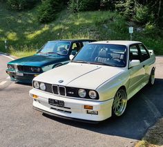 two cars parked next to each other on the side of a road with trees in the background