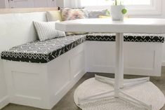 a white table and bench in a small room with pillows on the backrests