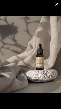 a bottle of essential oil sitting on top of a rock next to a white curtain