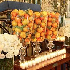 there are many vases filled with oranges and flowers on the table next to candles