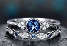 two wedding rings with blue and white diamonds on top of each other, sitting on a rock