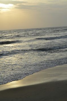 the sun is setting over the ocean with waves coming in