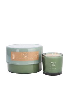 a candle that is sitting next to a glass jar with the words wild ferns on it