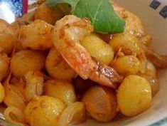 a bowl filled with shrimp and potatoes on top of a green leafy garnish