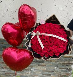 a bunch of red roses in a box with some heart shaped balloons next to it