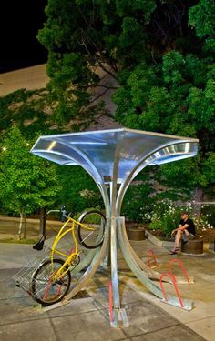 a man sitting on a bench next to a metal sculpture with a bike in it