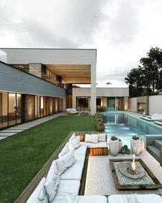 an outdoor living area with couches and tables next to a swimming pool in front of a house