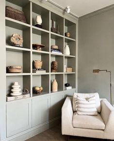 a white chair sitting in front of a book shelf filled with vases and other items