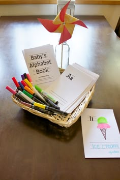 the baby's alphabet book is in a basket next to some pens and an origami pinwheel