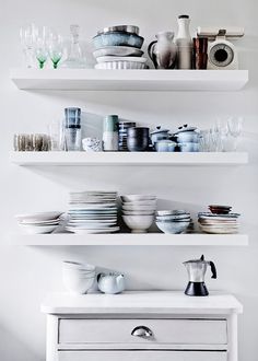 white shelves filled with dishes and cups on top of each other next to a dresser