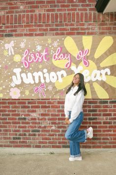 a woman standing in front of a brick wall with the words best day of junior year painted on it