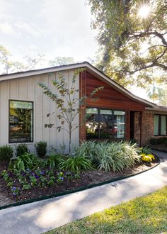 a small house with plants and flowers in the front yard, on a sunny day