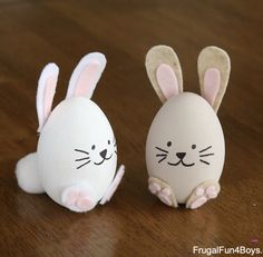 two stuffed rabbits sitting next to each other on a wooden table, one is white and the other has pink ears