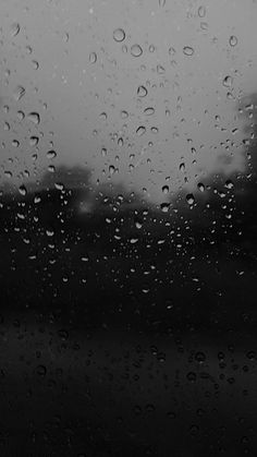 black and white photo of rain drops on the window with trees in the back ground