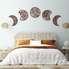 a bed with white sheets and pillows in front of three moon wall hangings on the wall