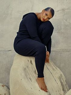 a woman sitting on top of a rock next to a cement wall with her hands behind her head