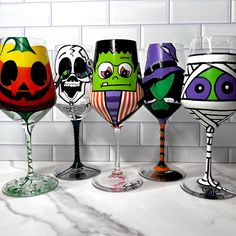 five wine glasses with painted faces on them are lined up against a white tile wall