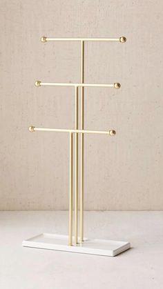 a three tiered gold metal rack on a white surface with beige wall in the background