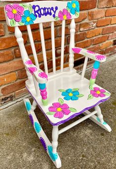 a child's rocking chair with flowers painted on the seat and name written on it