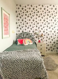 a bedroom with a bed, dresser and patterned wallpaper