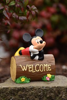 a mickey mouse figurine sitting on top of a log with the word welcome