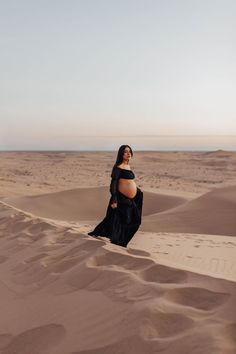 a pregnant woman sitting on top of a sand dune in the desert with her belly exposed