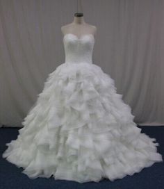 a white wedding dress with ruffled layers on the skirt is displayed in front of a curtain