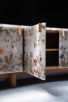 an artisticly designed cabinet with flowers painted on the doors and wood legs, in front of a black background