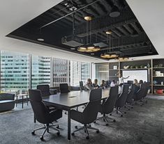 people are sitting around a conference table in an office setting with large windows and black chairs