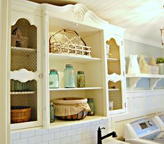 a white kitchen with lots of shelves and baskets on top of the cupboards in front of the sink