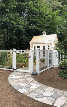 a white fenced in area with a small house on the other side and trees behind it