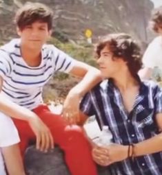 three young men sitting next to each other in front of a mountain side with trees