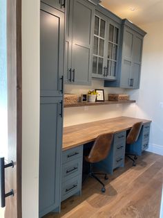 an office with gray cabinets and wooden desk in the center, along with two brown leather chairs